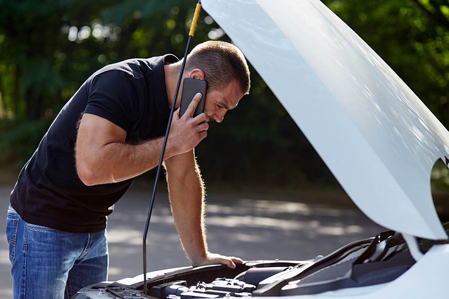 a man talks on the phone while looking under the hood of his car that is under an extended warranty