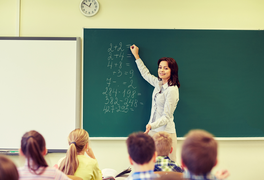 a teacher goes over common core math problems on the board in front of students in a classroom