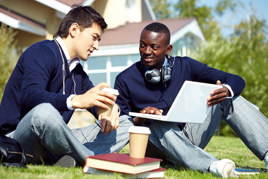 two students at a private school talk over textbooks while outside on the lawn