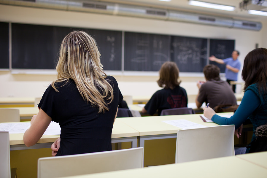 students in a classroom while an instructor points to the chalkboard