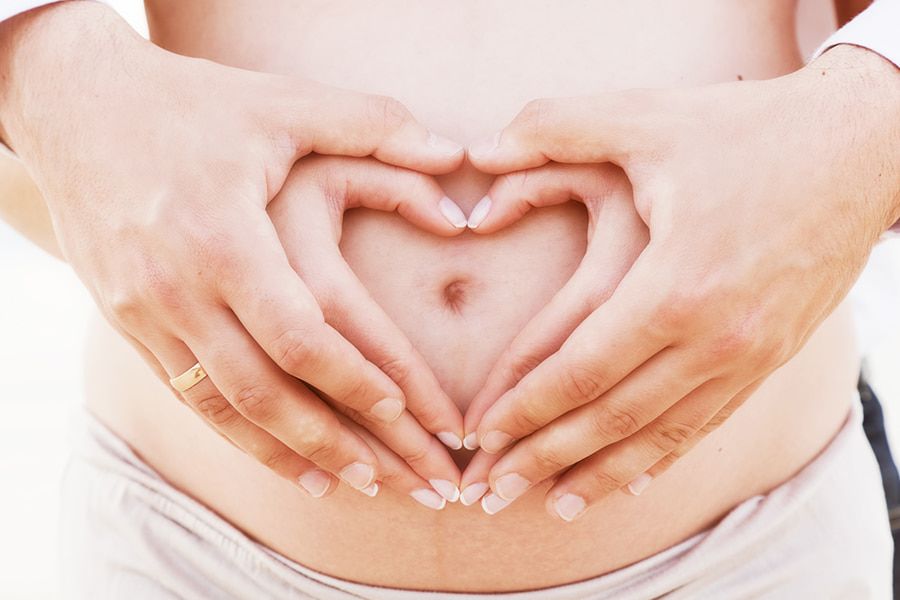 a pregnant woman makes a heart with her hands around her belly bump