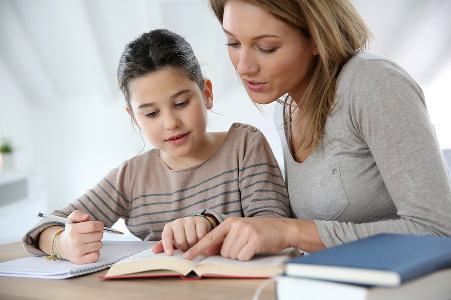 a mom homeschools her daughter at the counter while both pointing at a passage in a book