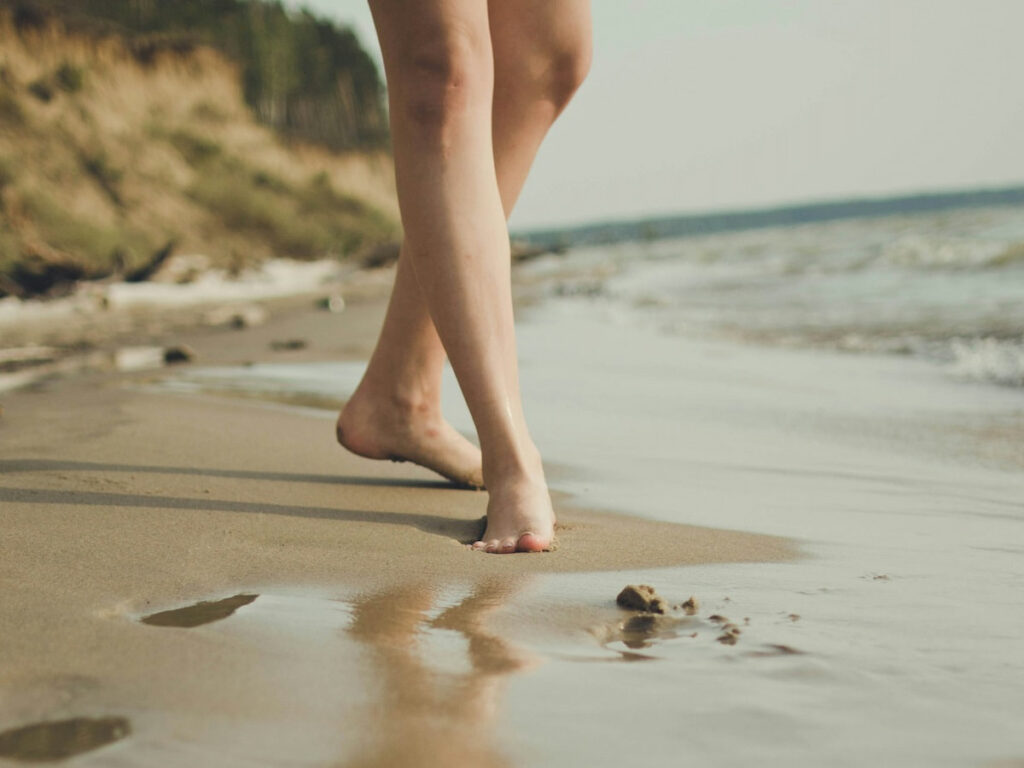 bare legs standing on the sand at the water's edge of a beach