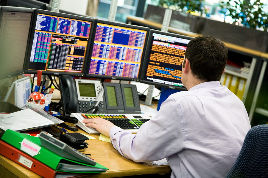 a man views monitors with financial information including hedge fund values