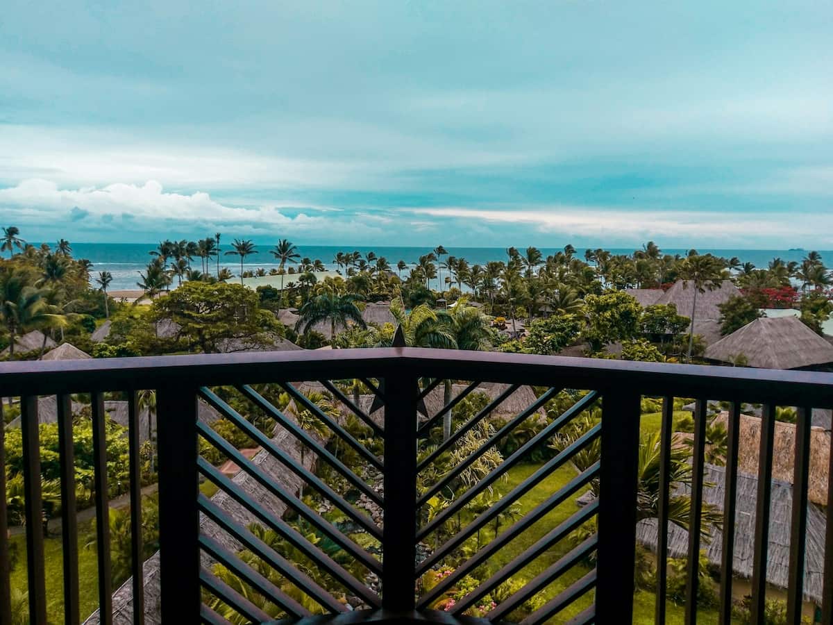 a view from a balcony in fiji of tropical trees and the ocean in the distance