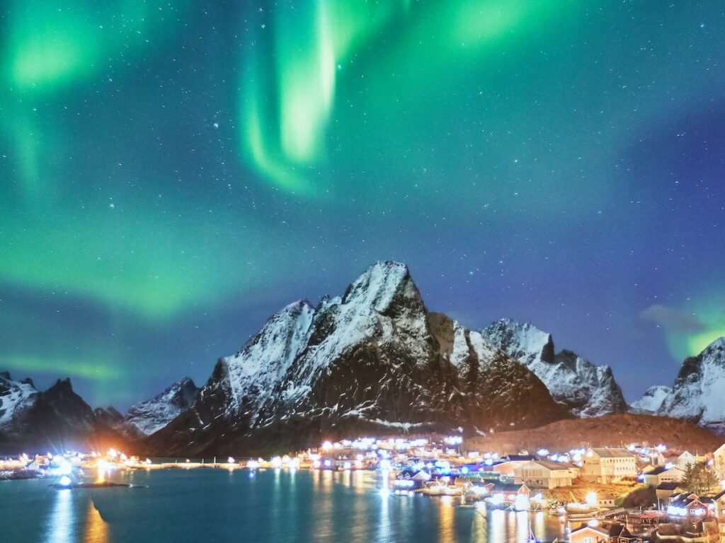green and white northern lights over a town at night at high northern latitudes
