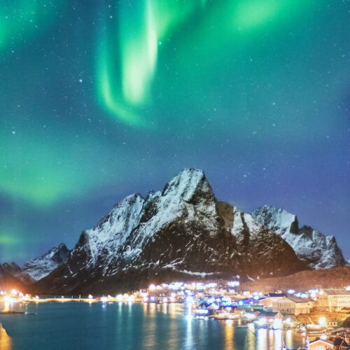 green and white northern lights over a town at night at high northern latitudes