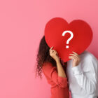 a man and woman holding a heart with a question mark on it.